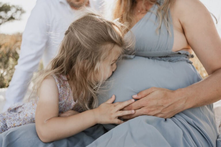 Mädchen küsst den Babybauch ihrer schwangeren Mutter bei einem Outdoor-Shooting bei Dresden