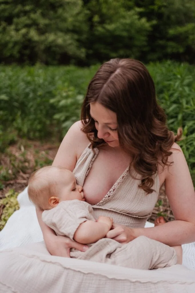 Mutter stillt ihr Baby sitzend auf einer Wiese